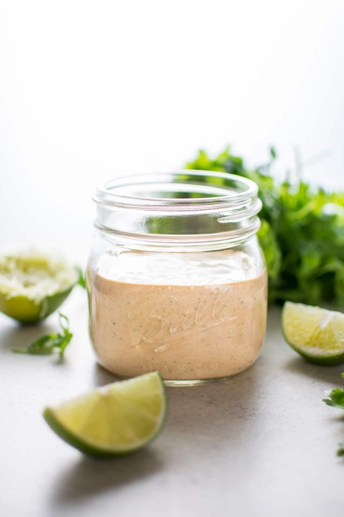 mason jar filled with chipotle ranch dressing beside lime wedges and cilantro bunch