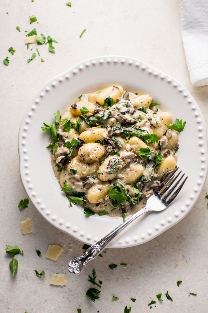 white bowl of creamy mushroom and spinach gnocchi with fork
