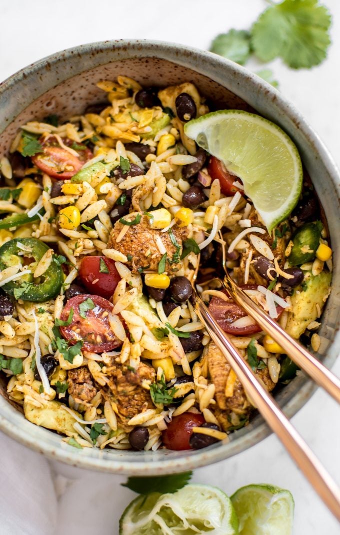 a bowl of Mexican orzo chicken salad with a lime wedge and utensils