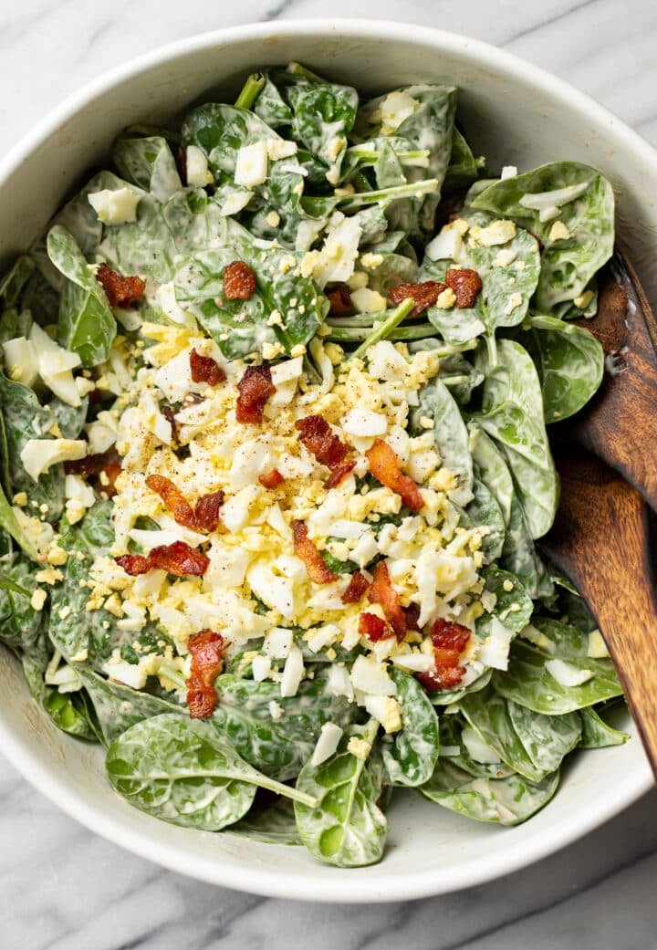 a bowl of spinach salad with serving spoons