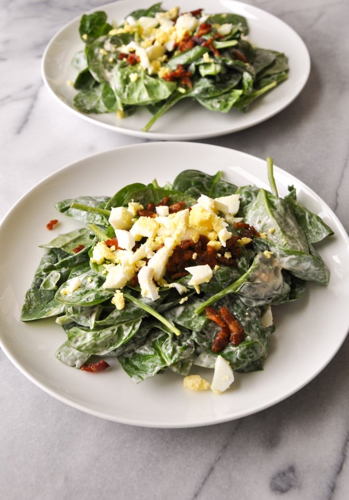 white plate of spinach salad with bacon and eggs with a tangy garlic dressing