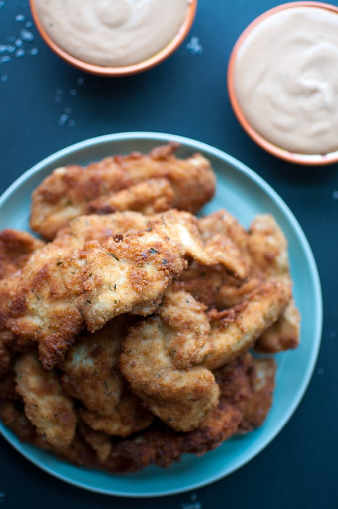 close-up of several breaded chicken tenders beside BBQ dip