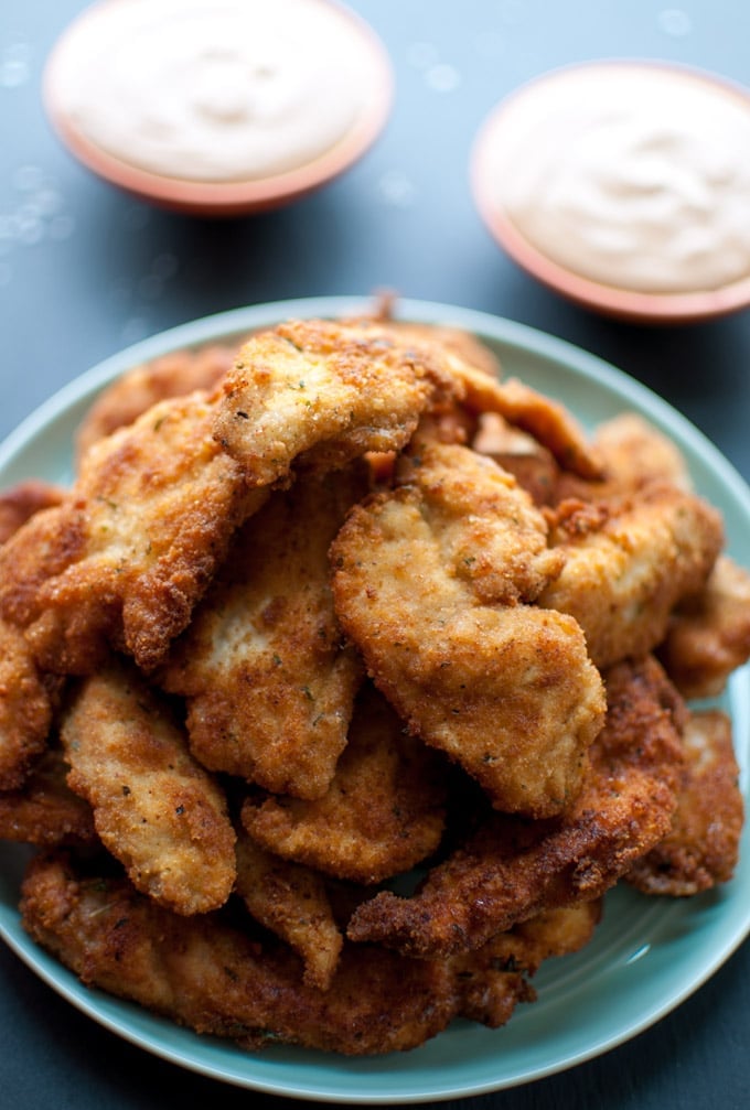 several breaded chicken tenders on a plate beside two small bowls of dip