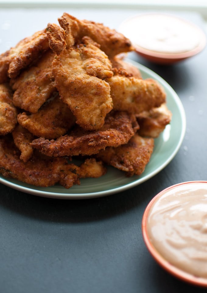 stack of breaded chicken tenders on a plate with close-up of dip in small bowl