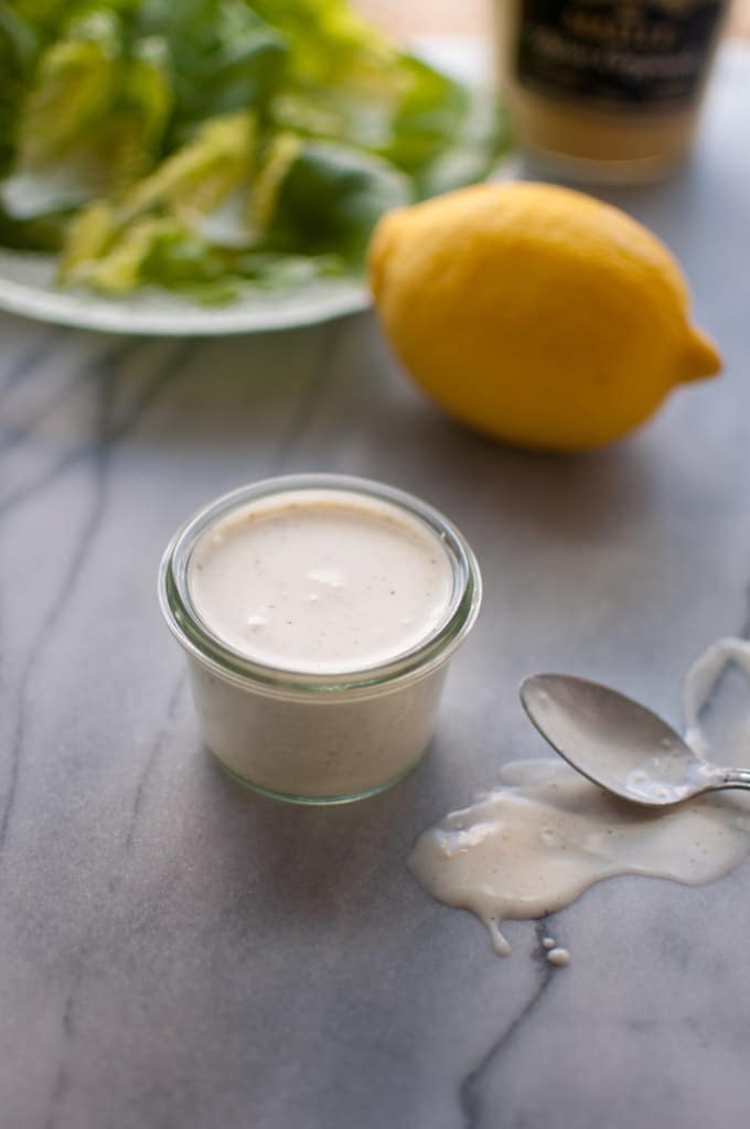 small glass jar with creamy lemon dressing beside a whole lemon and a spoon