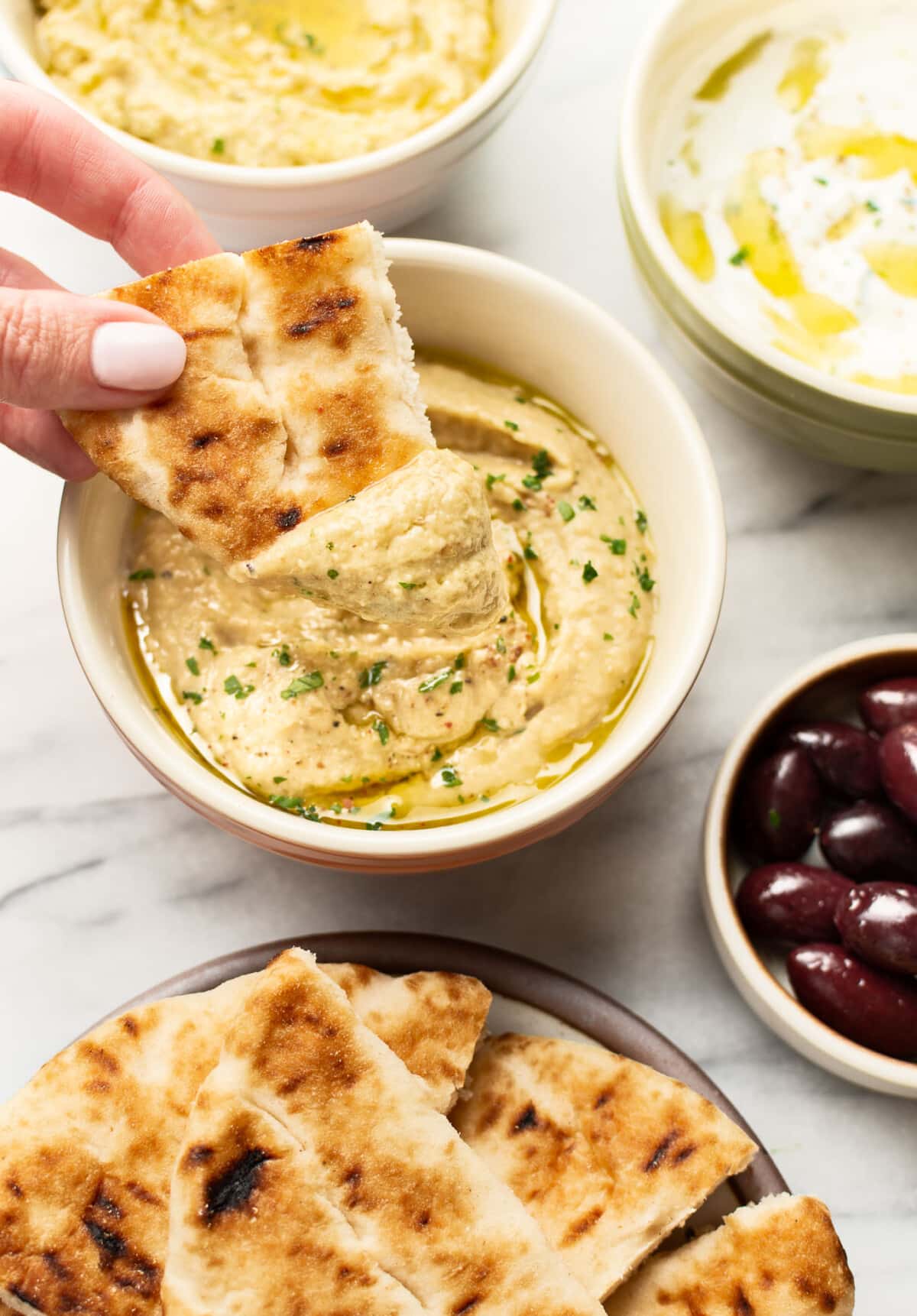 a female hand dipping pita into homemade greek eggplant dip
