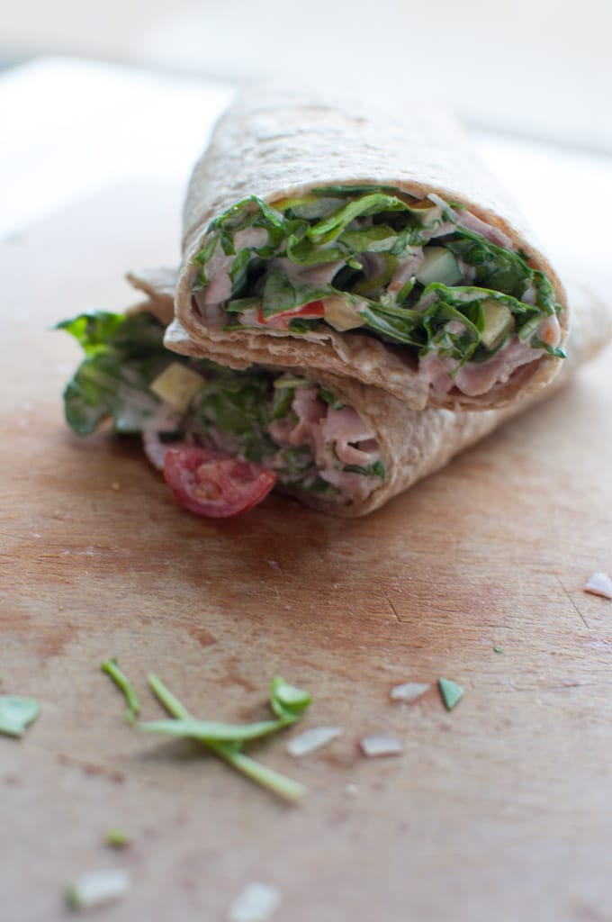two healthy ham wraps stacked on a cutting board