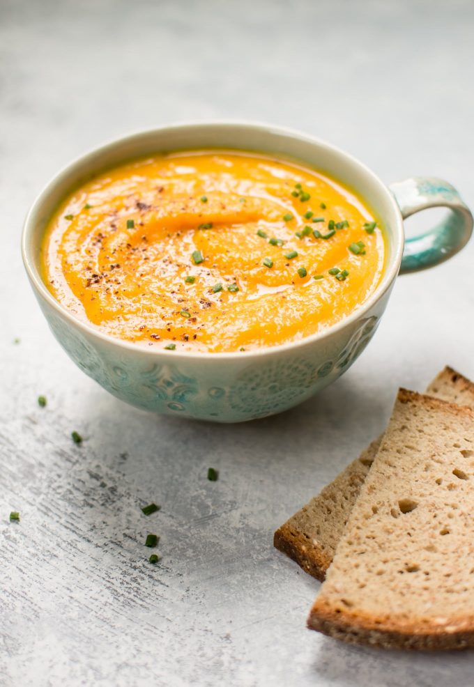 soup mug with vegetarian acorn squash and carrot soup beside rye bread slices