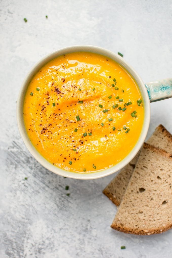 close-up of acorn squash carrot soup in a soup mug beside bread slices