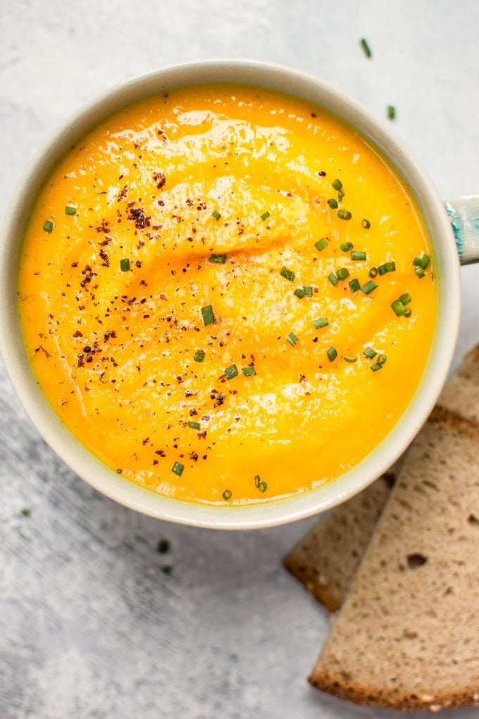 bowl of vegetarian acorn squash and carrot soup beside rye bread slices