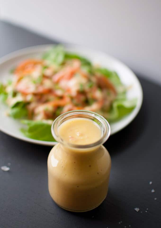 close-up of artichoke salad dressing in a glass jar with a bowl of salad in the background