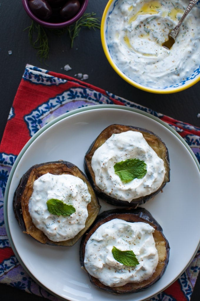 white plate with slices of easy fried eggplant with tzatziki and mint