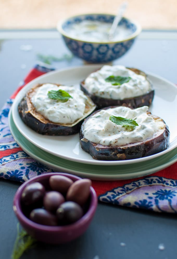 plate of three slices of easy fried eggplant topped with tzatziki and mint beside a bowl of olives