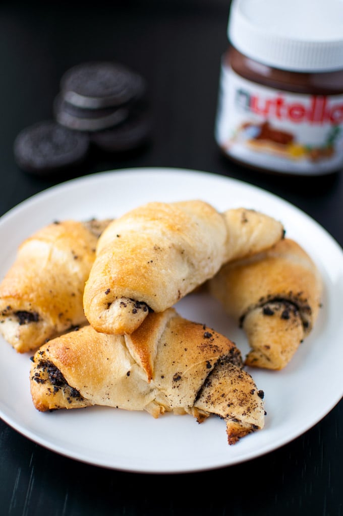 four Oreo and Nutella stuffed crescent rolls on a plate with Nutella jar and Oreos in the background