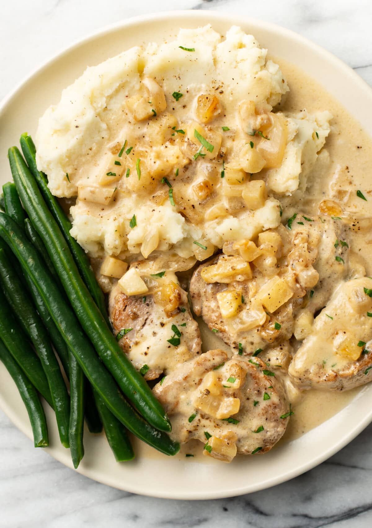 a plate with pork tenderloin in apple brandy sauce, mashed potatoes, and green beans