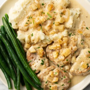 a plate with pork tenderloin in apple brandy sauce, mashed potatoes, and green beans