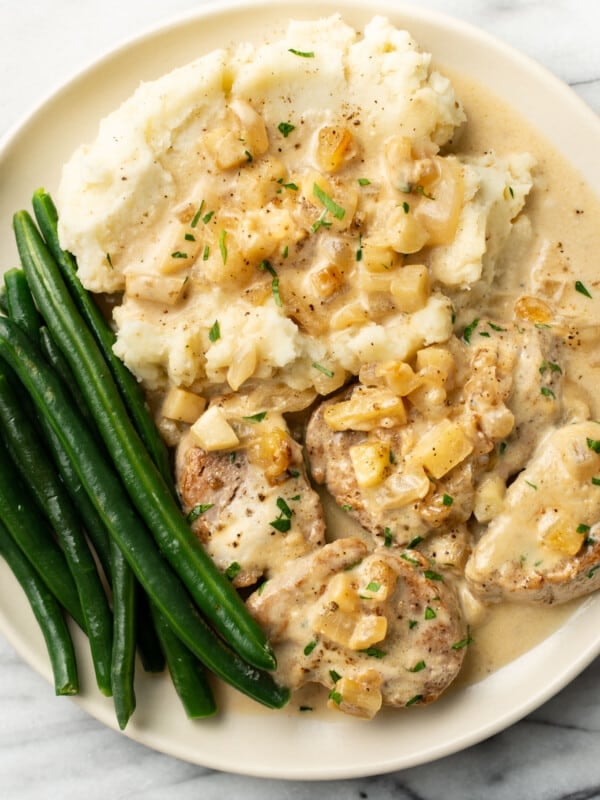 a plate with pork tenderloin in apple brandy sauce, mashed potatoes, and green beans