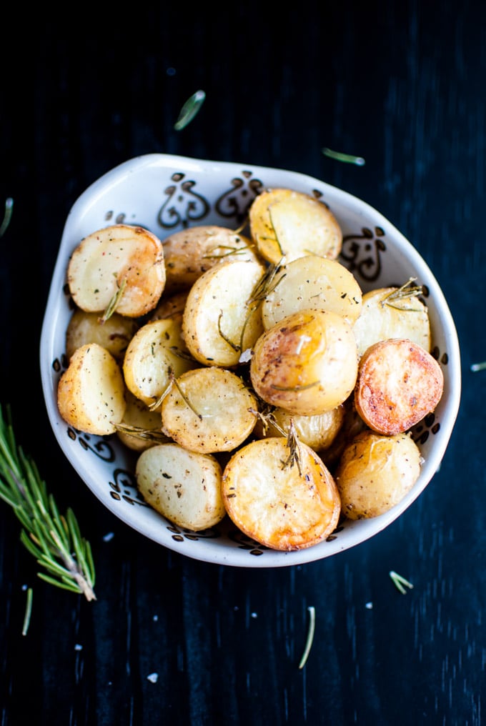 bowl of rosemary roasted potatoes with a sprig of rosemary