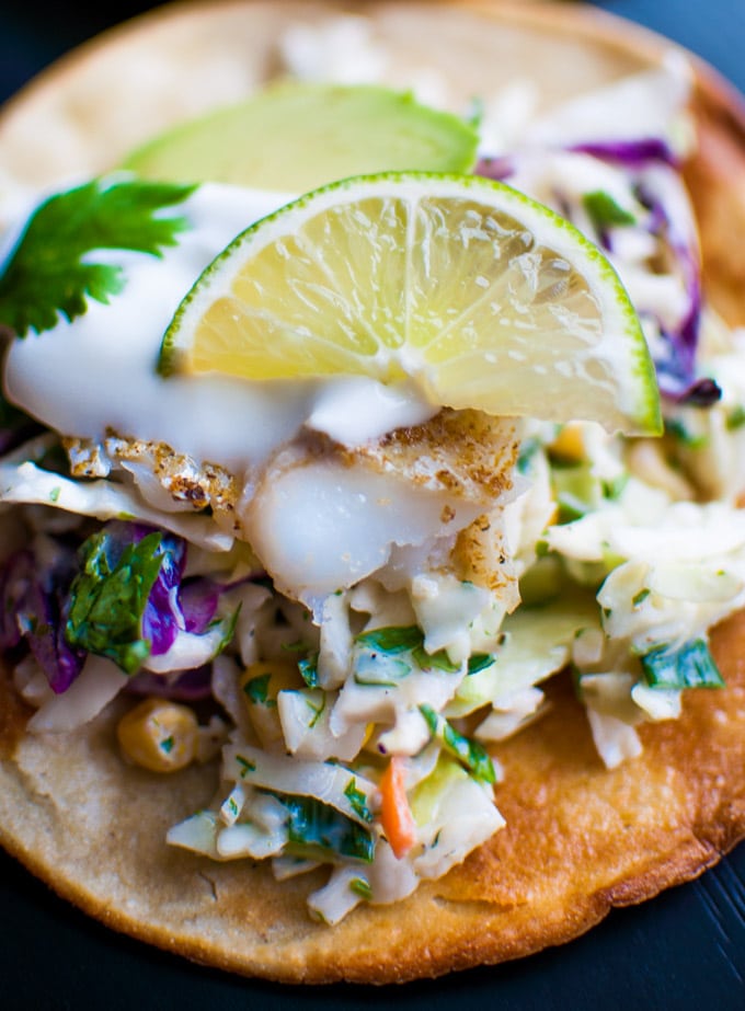 close-up of fish tostada with sour cream, avocado, and lime garnish