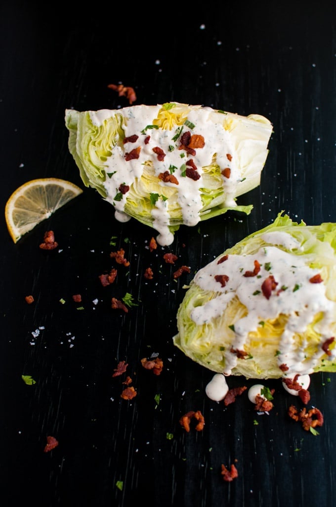 two iceberg lettuce wedges with ranch and bacon dressing and lemon slice