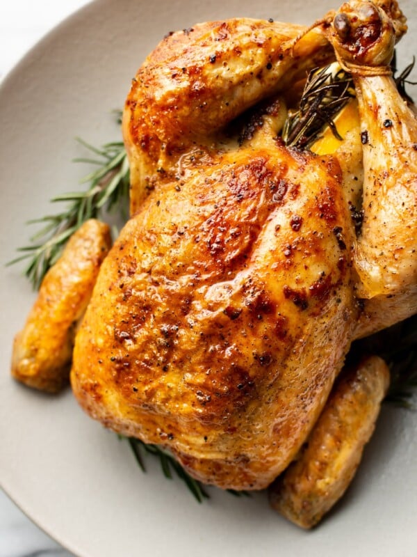 close-up of cooked crispy whole roast chicken in a shallow bowl surrounded by fresh rosemary