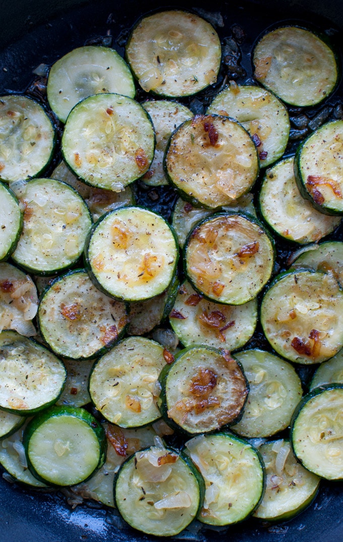 close-up of several slices of zucchini with sauteed onions in a skillet