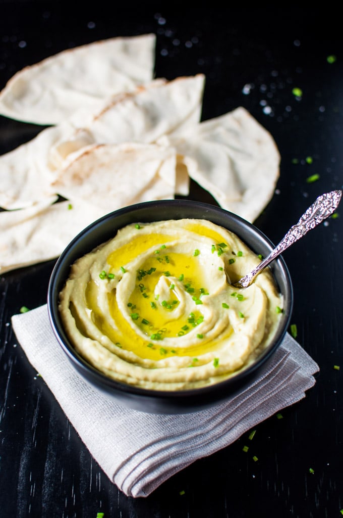 black bowl of healthy avocado and white bean dip appetizer with spoon beside pita bread slices