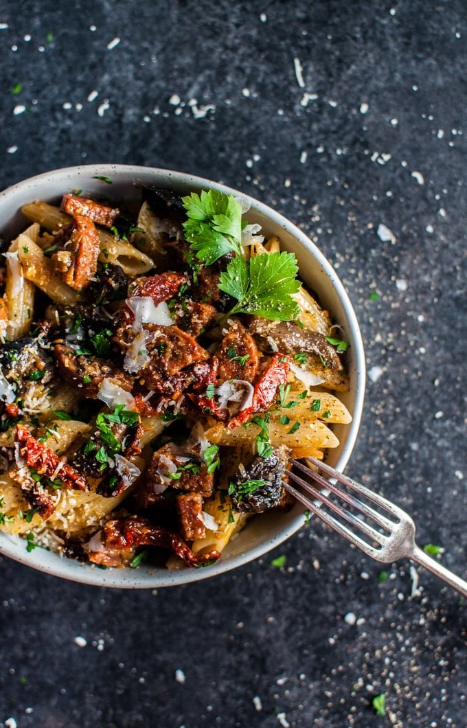 white bowl with chorizo pasta with mushrooms, garlic, and sun-dried tomatoes and a fork