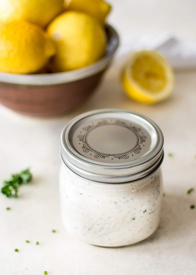 healthy ranch dressing inside a mason jar with lid with a bowl of lemons behind