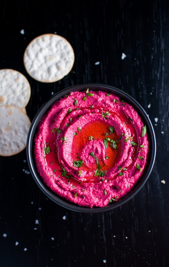 black bowl with roasted beet hummus topped with parsley and olive oil beside crackers