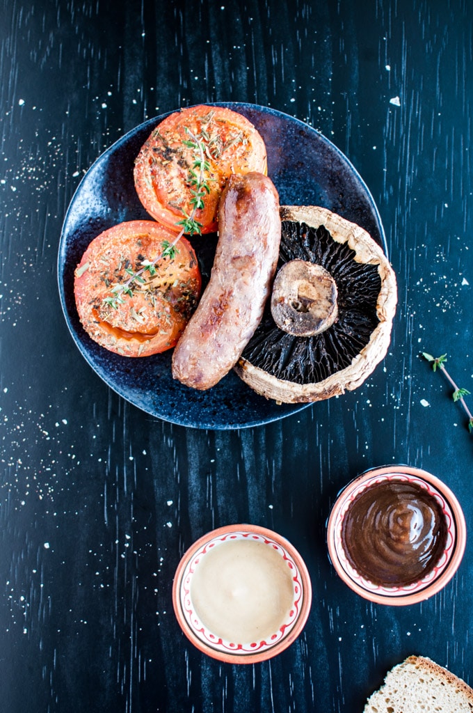 plate of roasted sausages, tomatoes, and portobello mushrooms with bowls of dipping sauces