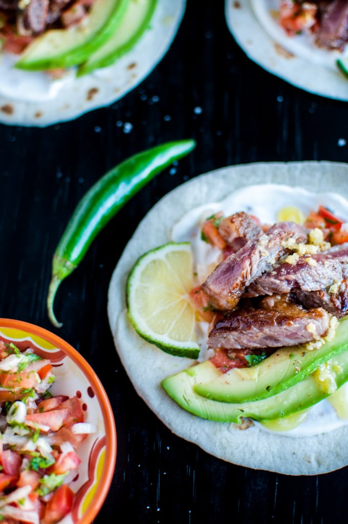 garlic butter steak taco beside a whole chili and a bowl of homemade pico de gallo