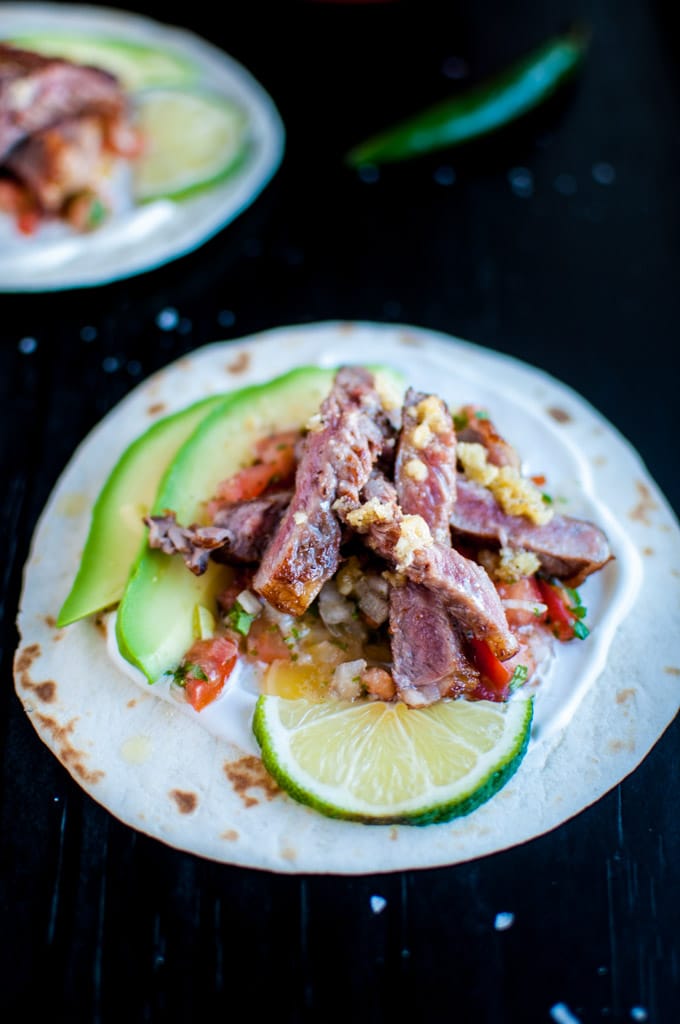 a garlic butter steak taco with homemade pico de gallo, avocado slices, and a lime slice