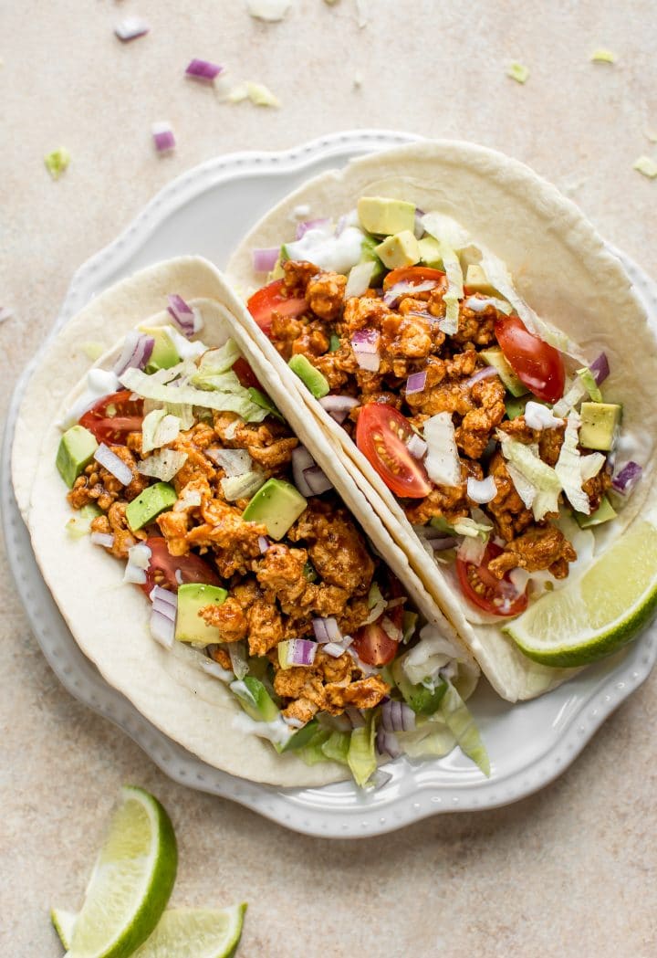 white plate with two BBQ chicken tacos with ground chicken, avocado, sour cream, onions, and lettuce