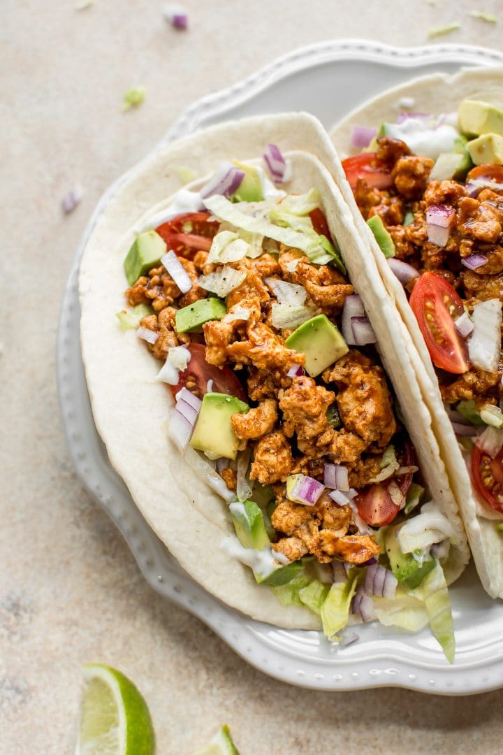 close-up of BBQ chicken tacos with sour cream, onions, iceberg lettuce, and tomatoes on a plate