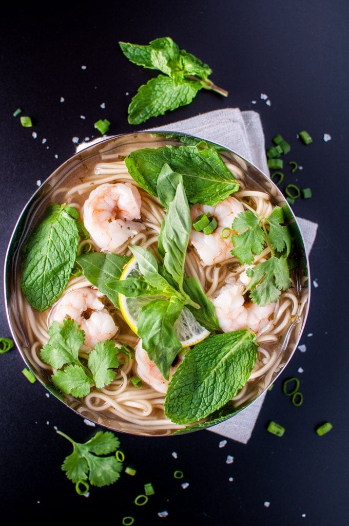 Asian-style shrimp and noodle soup in a metal bowl with mint and cilantro garnish