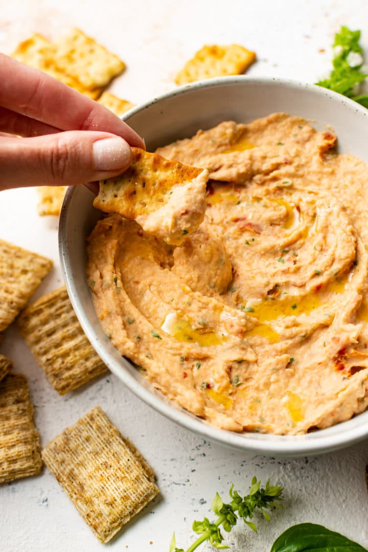 close-up of a cracker being dipped into cannellini bean dip