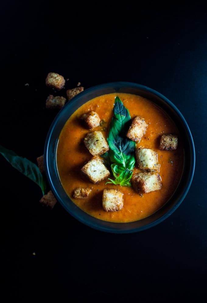 black bowl of easy tomato soup garnished with sage croutons and basil