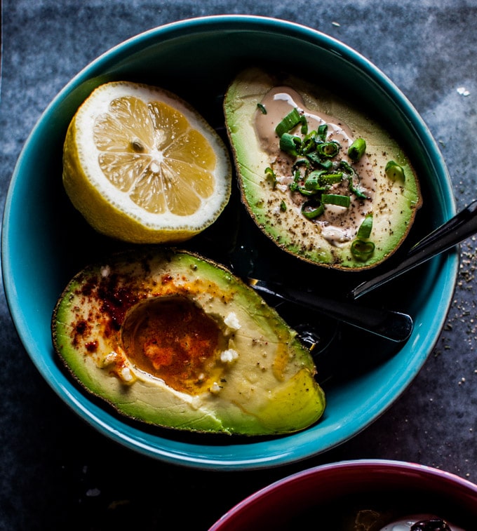 two avocado halves in a blue bowl with a lemon wedge