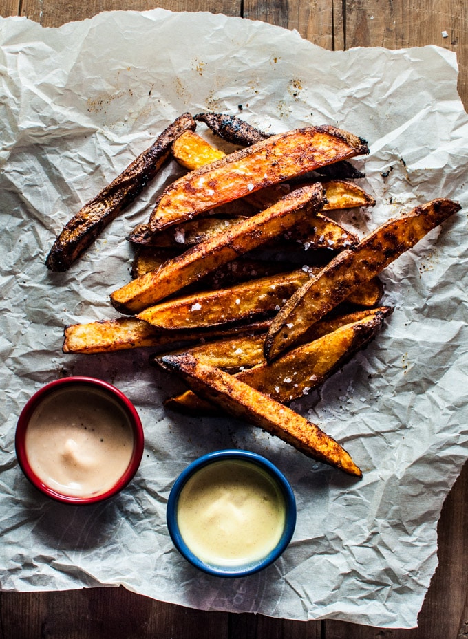 pile of beer oven fries with smoked paprika on parchment paper with two bowls of honey Dijon and BBQ mayo dipping sauce