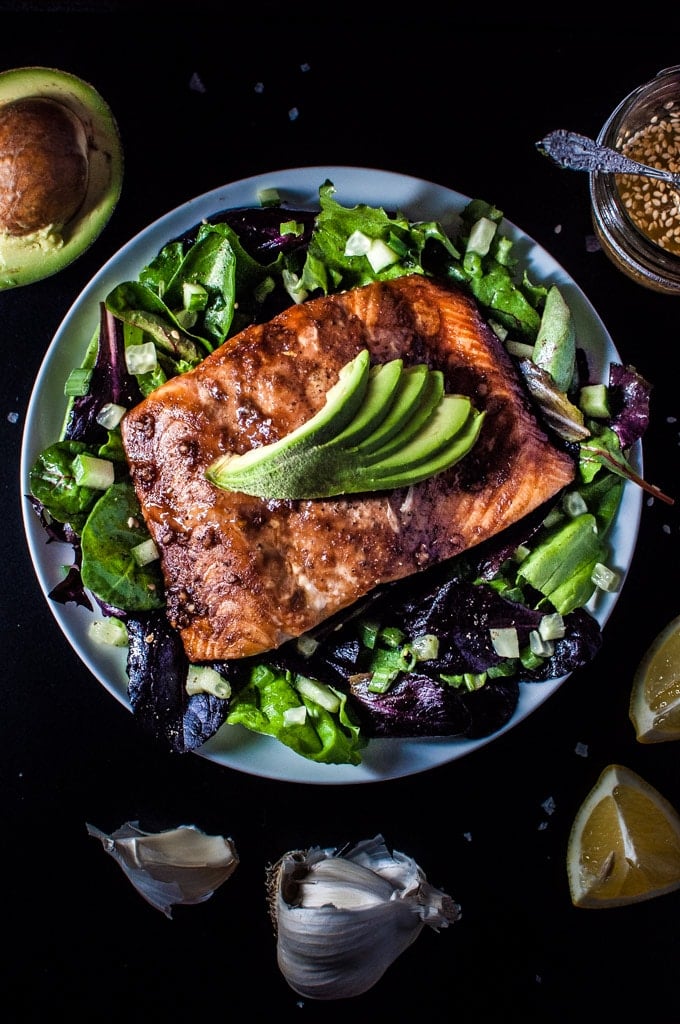 blue plate with salmon salad with spinach and a toasted sesame seed dressing topped with avocado slices