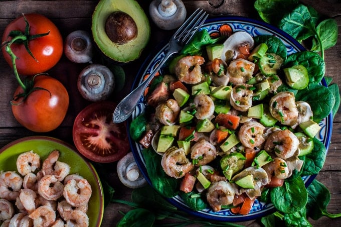 plate with spinach salad with shrimp and a smoky sweet dressing with several ingredients beside it