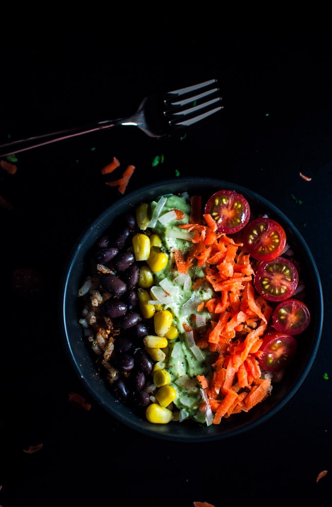 A Tex-Mex rice bowl with carrots, tomatoes, cucumber, corn, and beans beside a fork