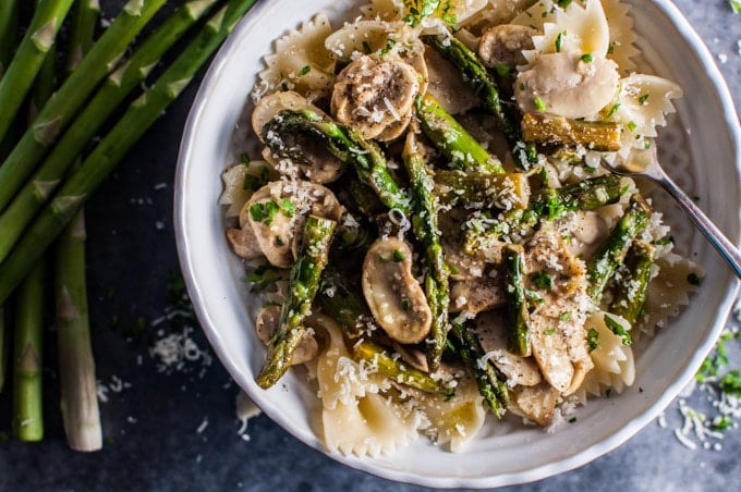 close-up of healthy asparagus and mushroom bow tie pasta in a white bowl with grated parmesan