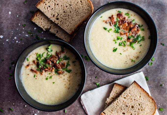 two bowls of low-carb cauliflower and leek soup beside slices of rye bread