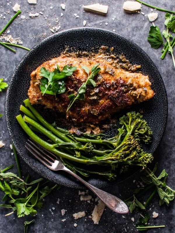 parmesan crusted chicken breast on a black plate with broccolini and a fork