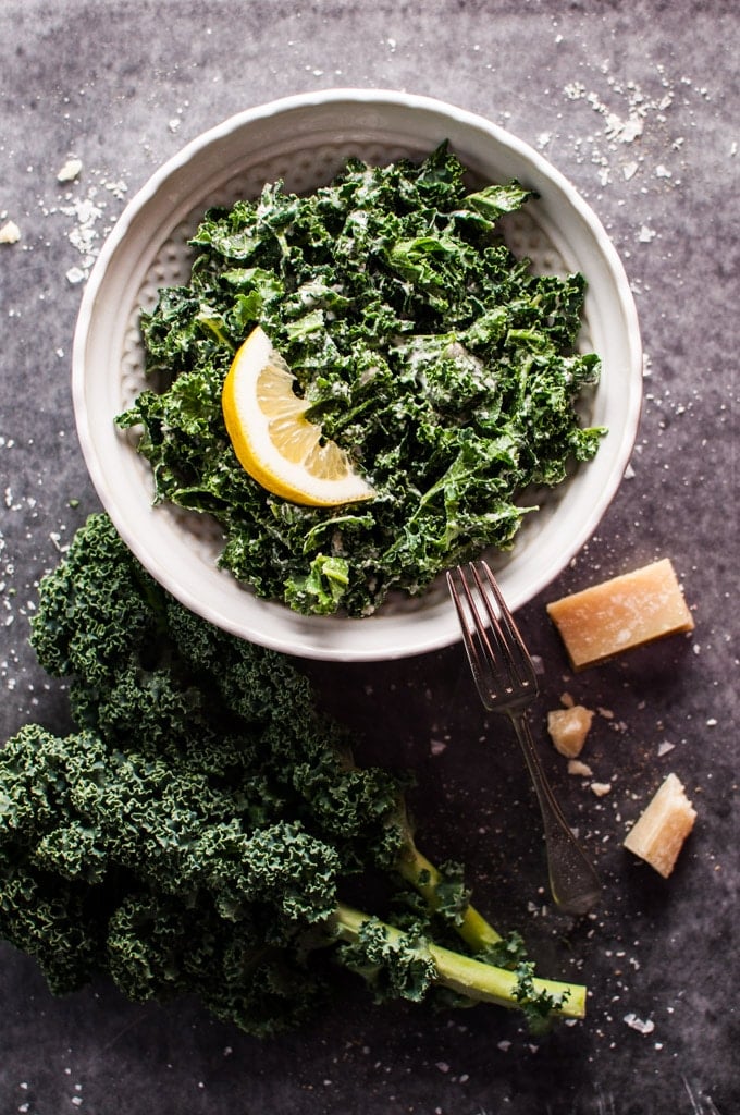 a white bowl of kale salad with parmesan, lemon, and black truffle oil with a fork