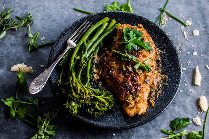 plate with parmesan chicken breasts with herb sauce on a plate with broccolini