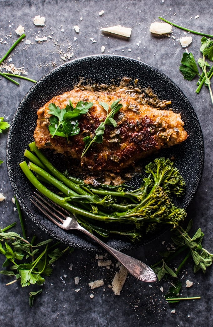 parmesan crusted chicken breasts with a fresh herb sauce on a plate with broccolini and a fork