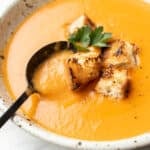 a bowl of potato leek tomato soup with croutons and a spoon